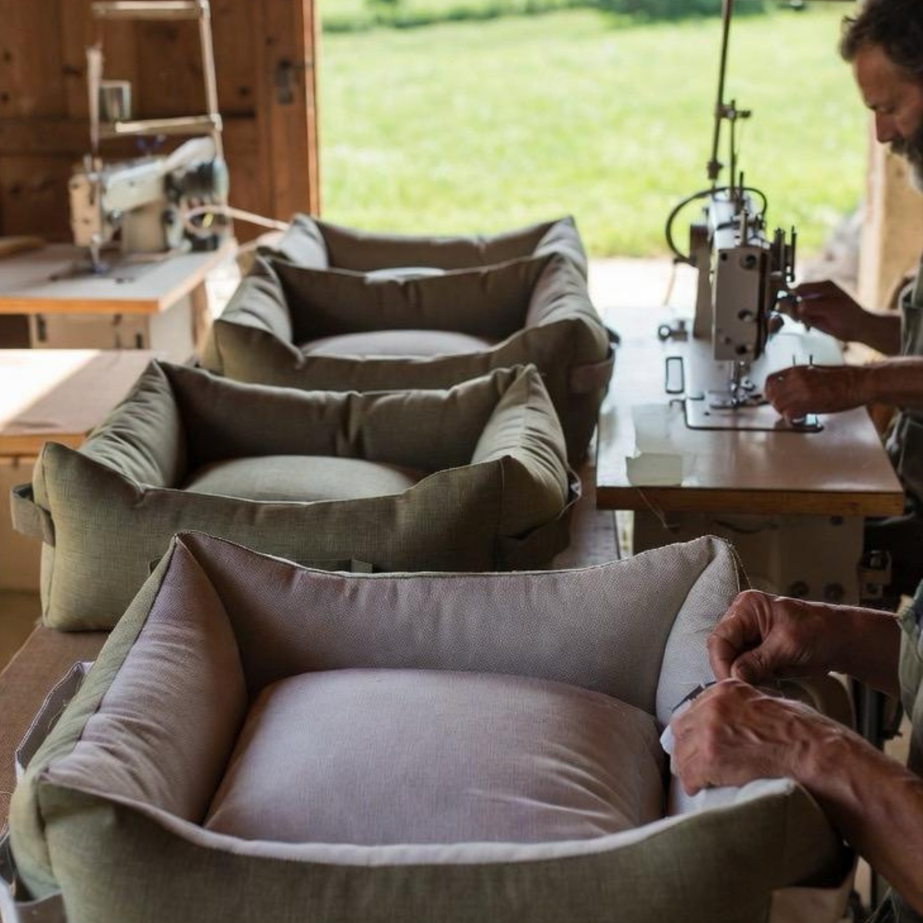Row of finished luxury pet beds with craftsman at sewing machine